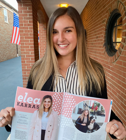 A woman holding a magazine in front of a brick building.